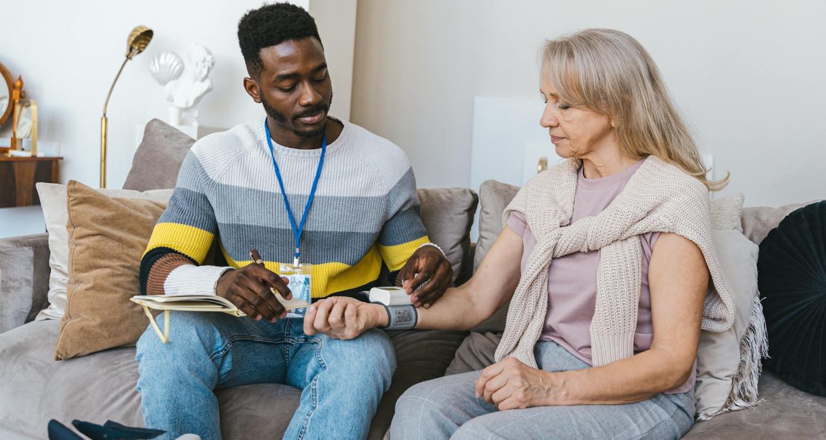 Volunteer checking elderly woman's blood pressure at home. Compassionate healthcare support.